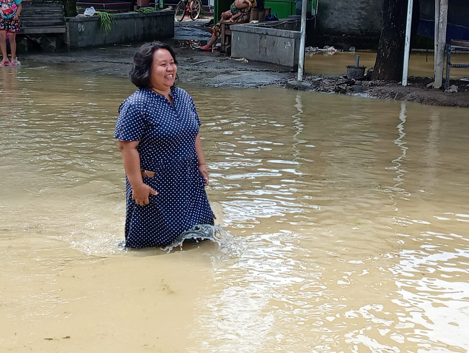 Seorang warga melintas di tengah jalan yang banjir