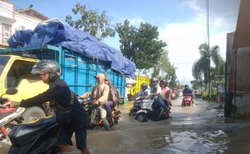 Foto: Tampak pengendara motor sedang berjuang melewati jalan banjir