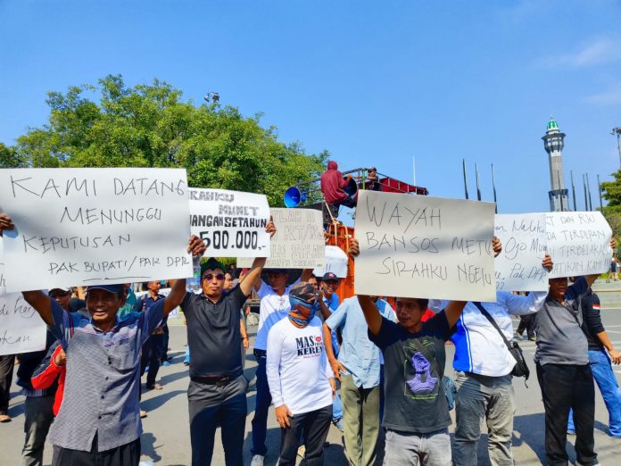 Massa aksi RT - RW membawa poster dengan berbagai tulisan di depan kantor Bupati Pati, Kamis (22/6/2023)